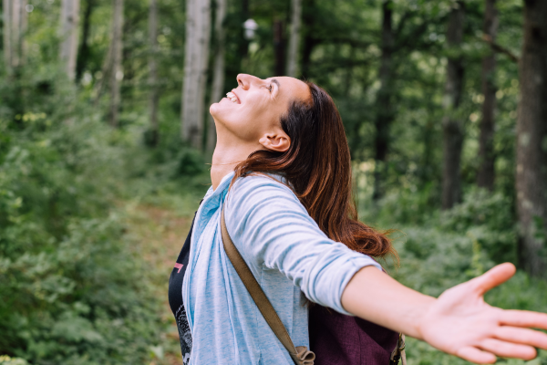 woman putting her head back and arms out in the woods