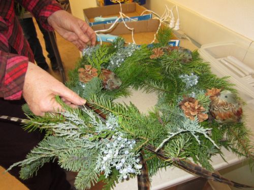 Hands adding greens to an evergreen wreath with pine cones.